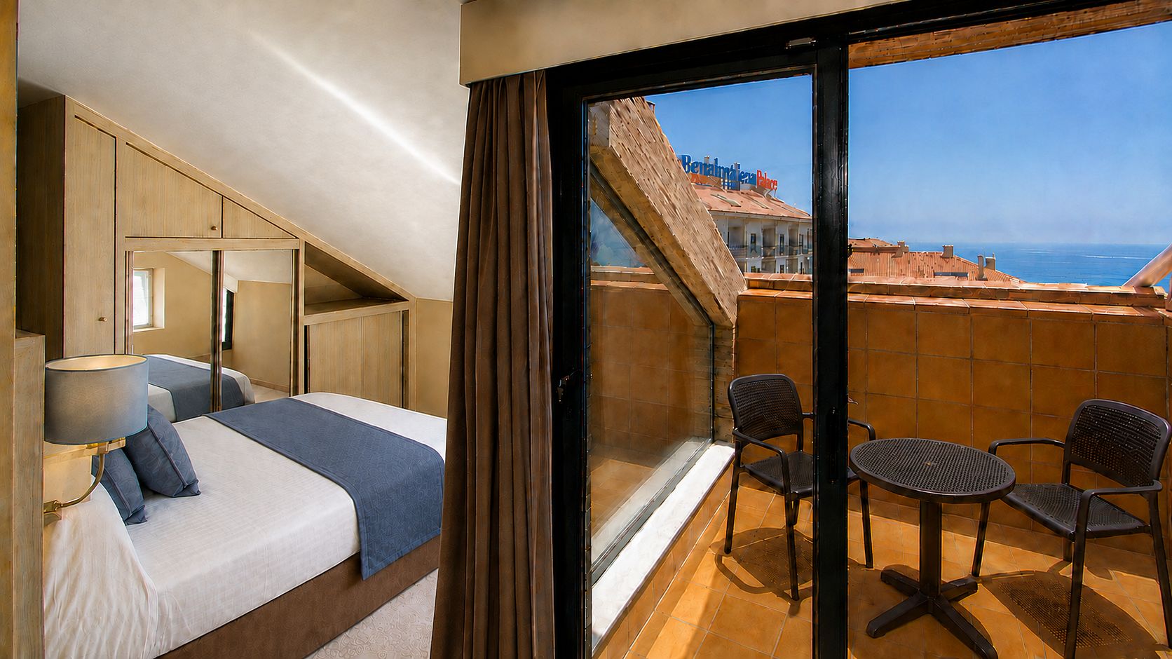 A hotel room with a bed, a desk, and a balcony with chairs and a table.
