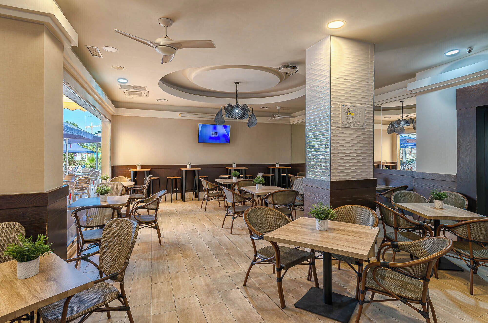 A restaurant interior with multiple tables and chairs, ceiling fans, and a TV mounted on the wall.