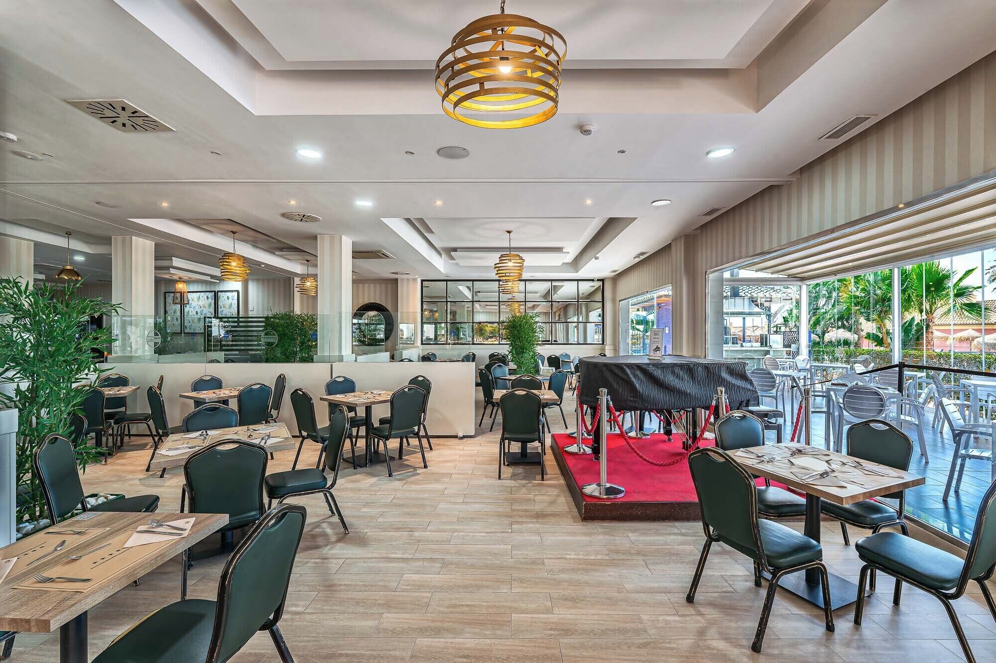 A restaurant with a modern interior, featuring wooden tables and chairs, a red carpet area, and large windows offering a view of the outdoors.