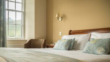 A neatly made bed with floral pillows, a wooden headboard, a nightstand, and a wall-mounted lamp.
