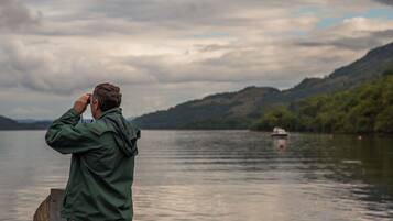 Una persona fotografiando un lago, con un barco a lo lejos y colinas al fondo.
