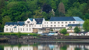 Un grand bâtiment blanc, doté de nombreuses fenêtres et d’un toit végétalisé, situé au bord d’une étendue d’eau calme.