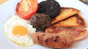 A plate with a fried egg, sausage, black pudding, grilled tomato, and fried hash browns.