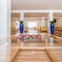 A spacious lobby with a central glass table, seating areas, and decorative plants.