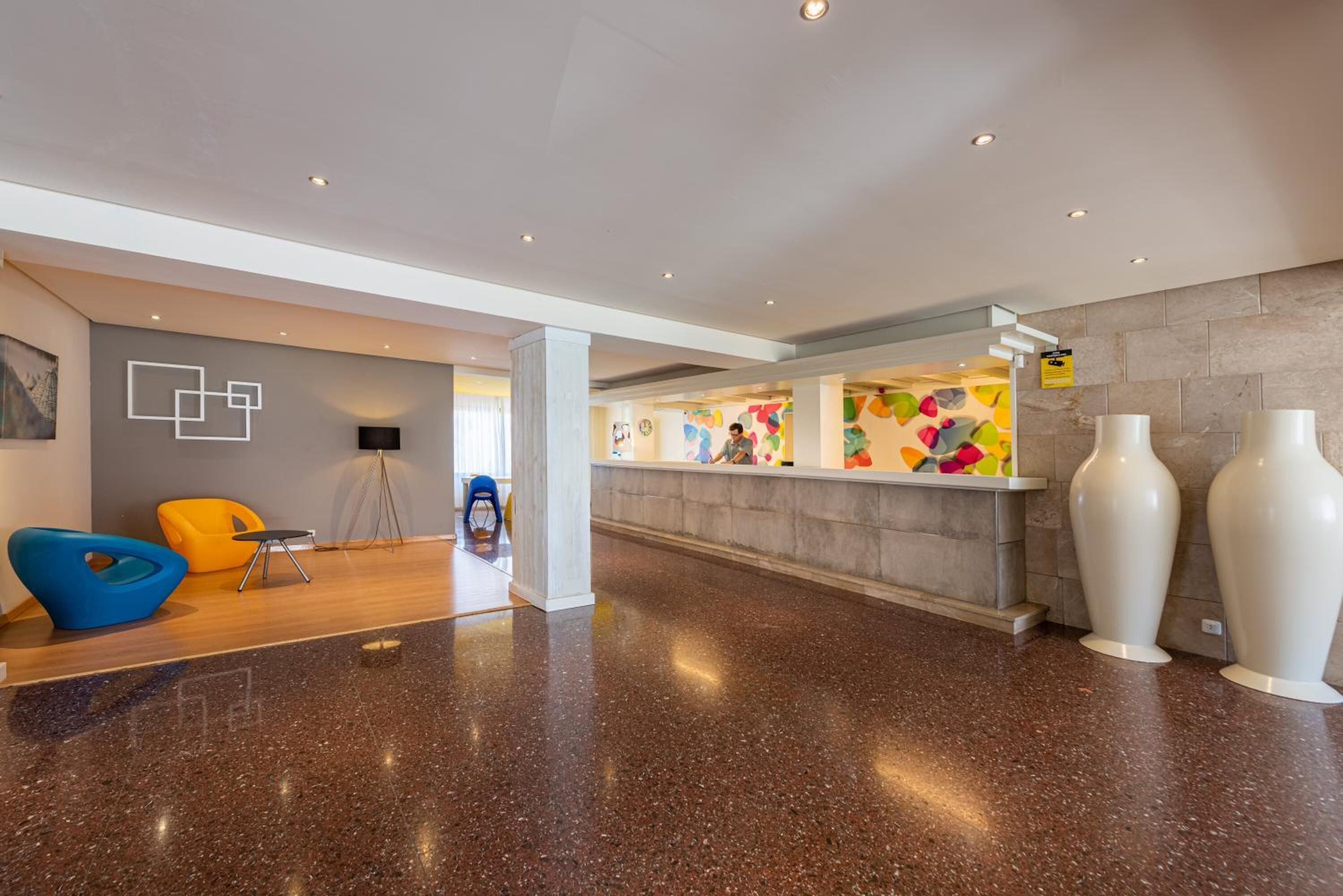 Un hall d’entrée doté d’un sol en granit poli, d’un comptoir de réception, d’œuvres d’art colorées sur les murs et de mobilier moderne.