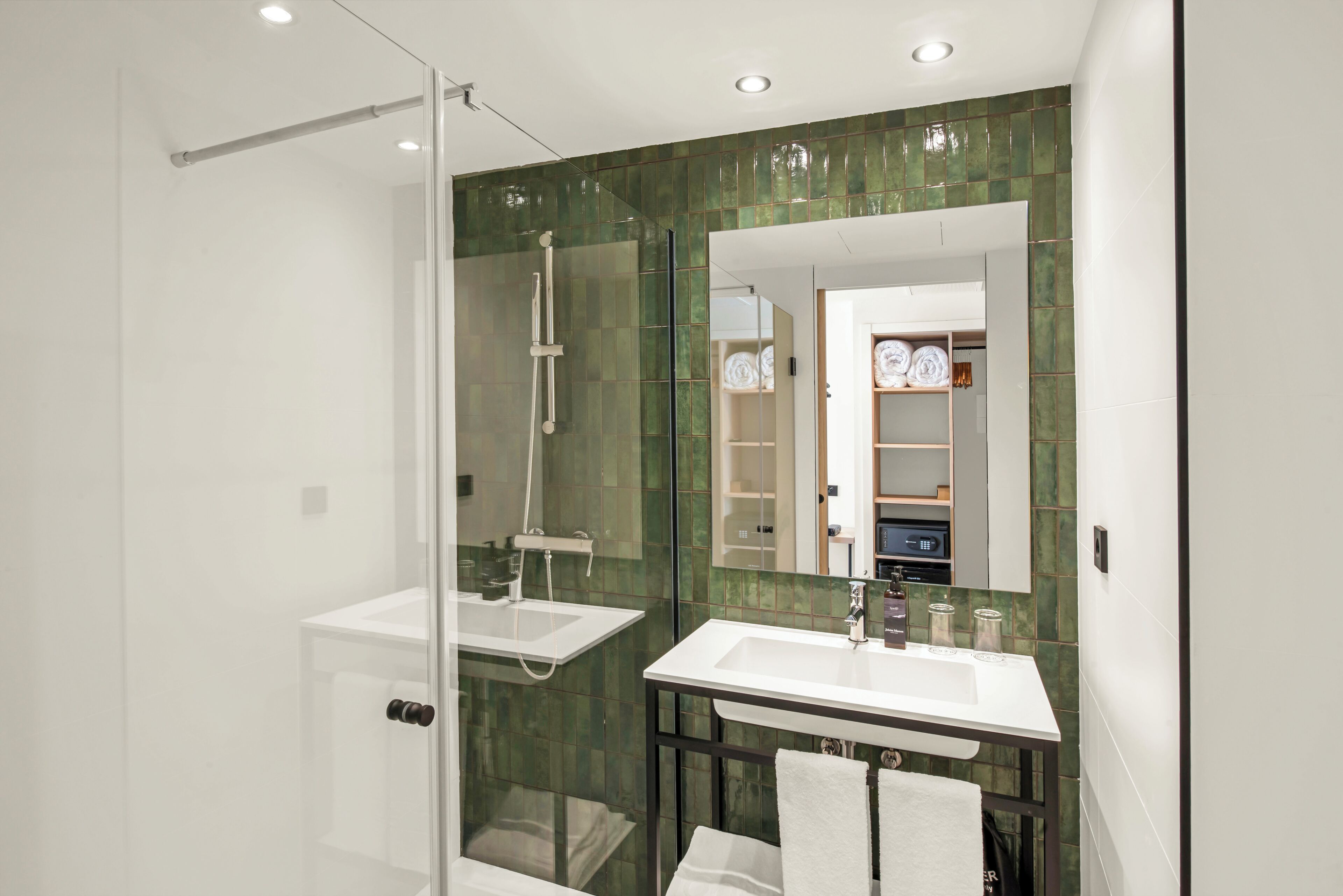 Un baño moderno con cabina de ducha de vidrio, lavabo blanco y un espejo que refleja un mueble de tocador.