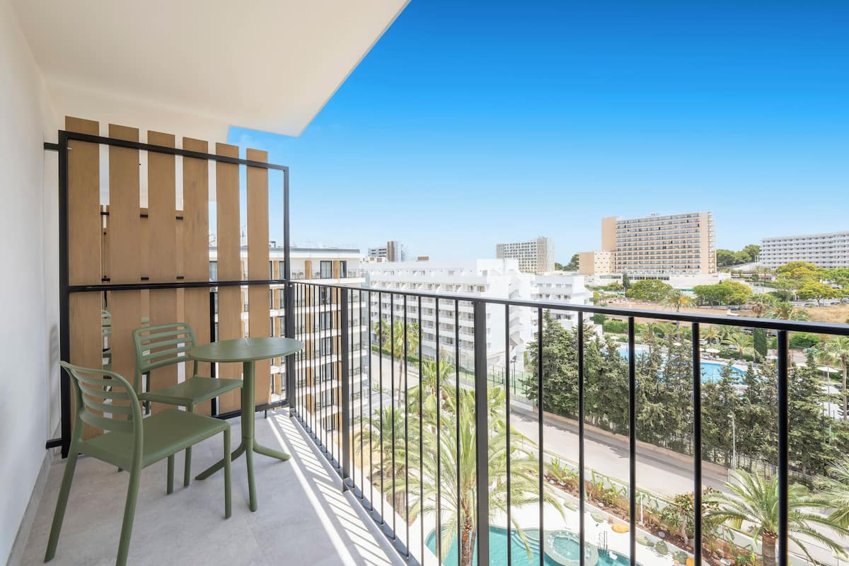 A balcony with a table and chairs, a view of a swimming pool, and surrounding buildings.