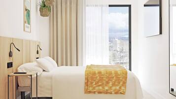 A modern hotel room with a bed, a nightstand, a wall-mounted lamp, a window with a city view, and a poster on the wall.