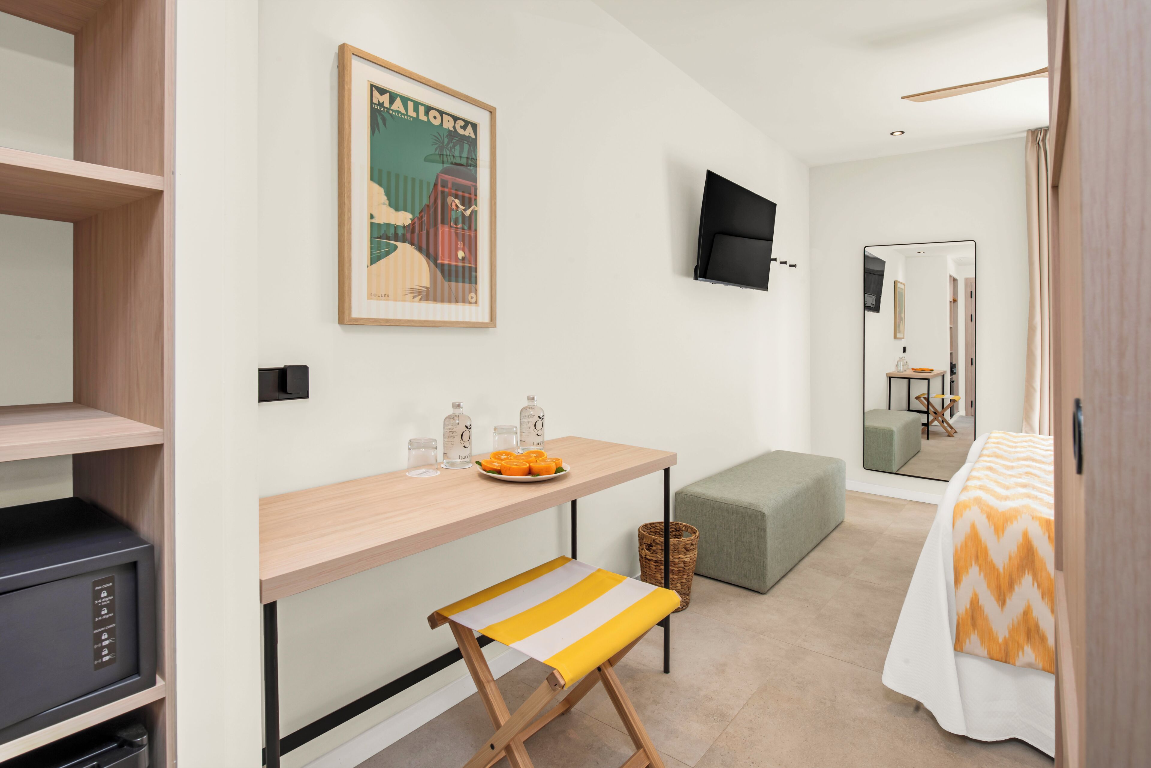 A hotel room with a bed, a small table with a bench, a television, a framed picture on the wall, and a mirror.