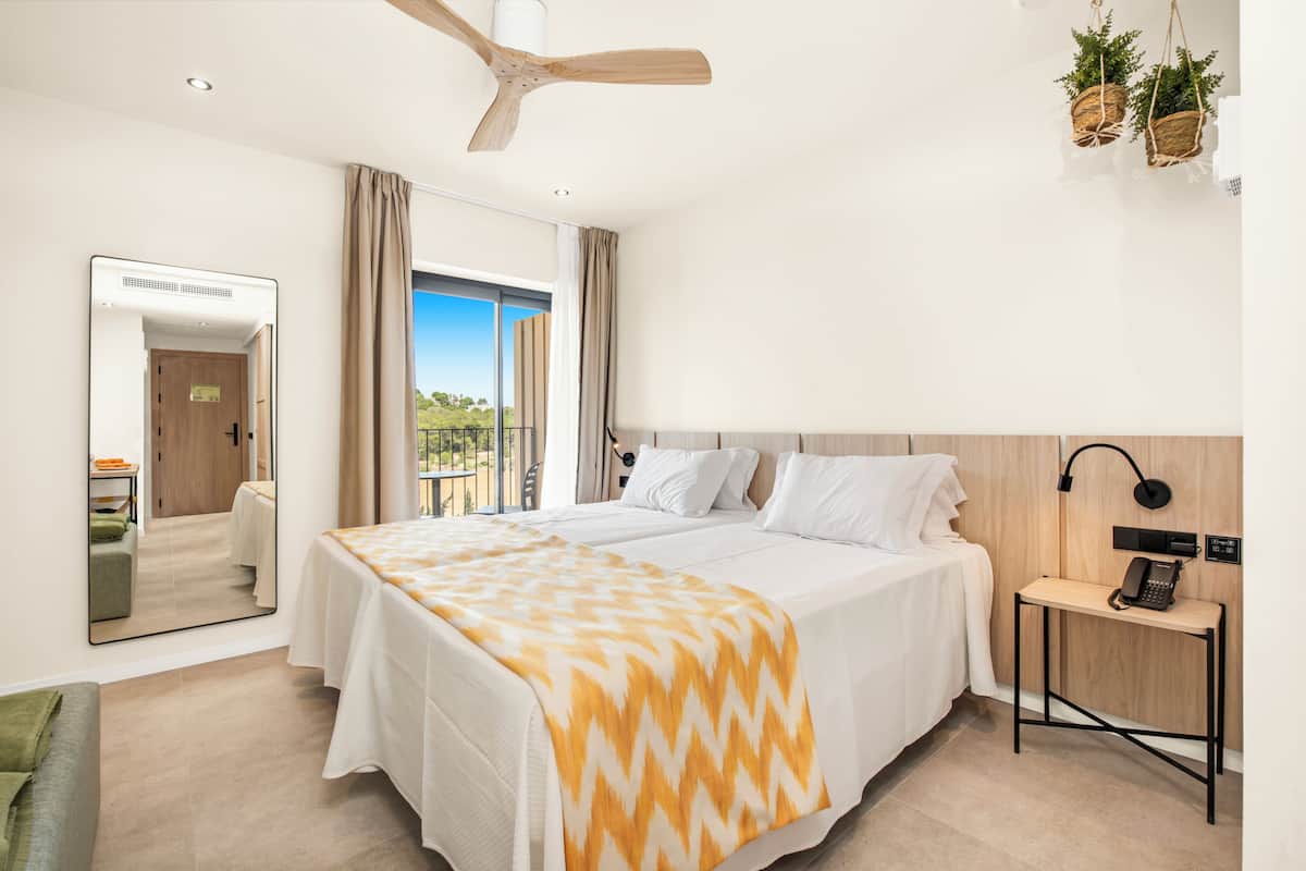 A hotel room with a bed, bedside table, and a view of the outdoors.