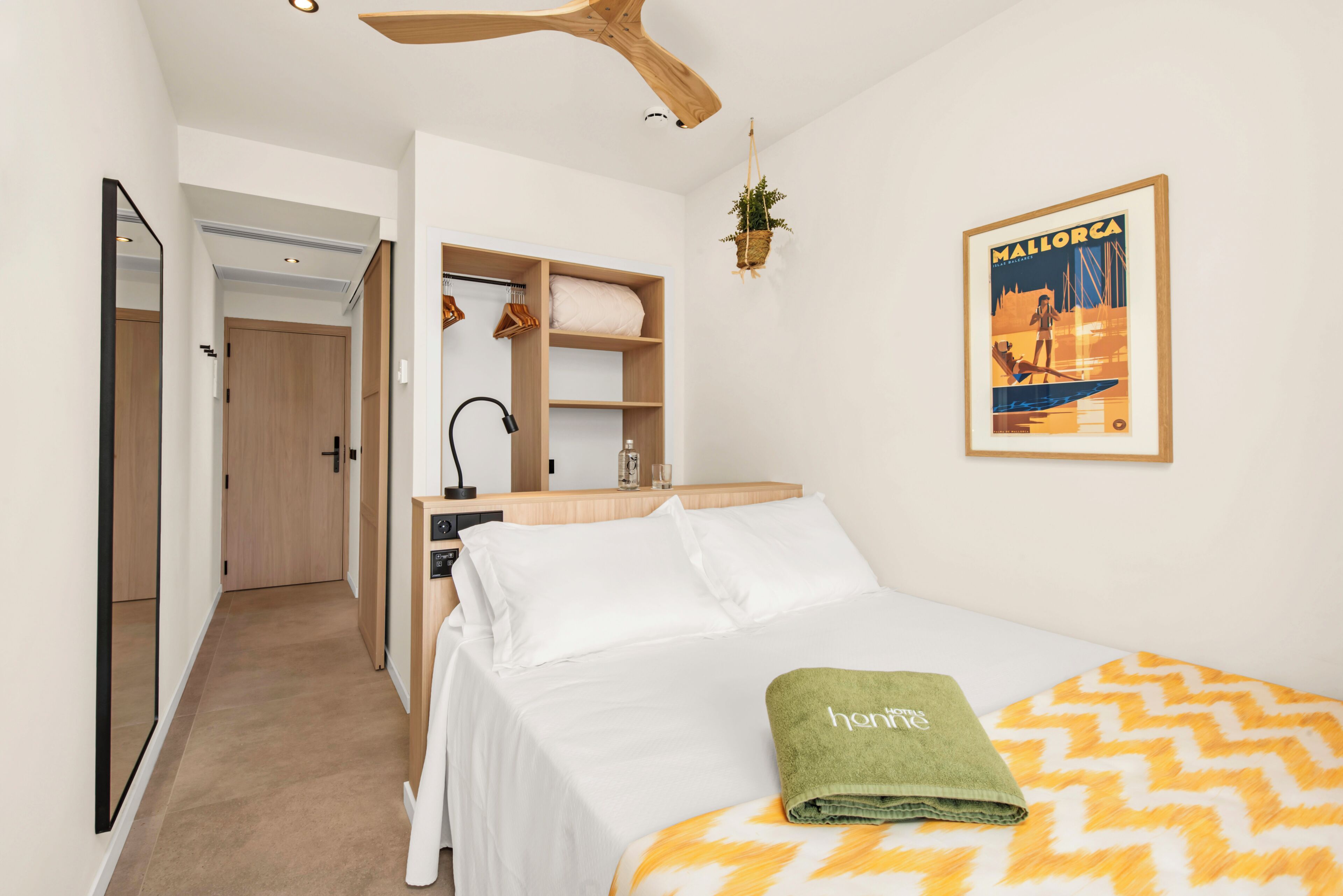 Habitación de hotel con cama, escritorio, silla, planta colgante e imagen enmarcada en la pared.