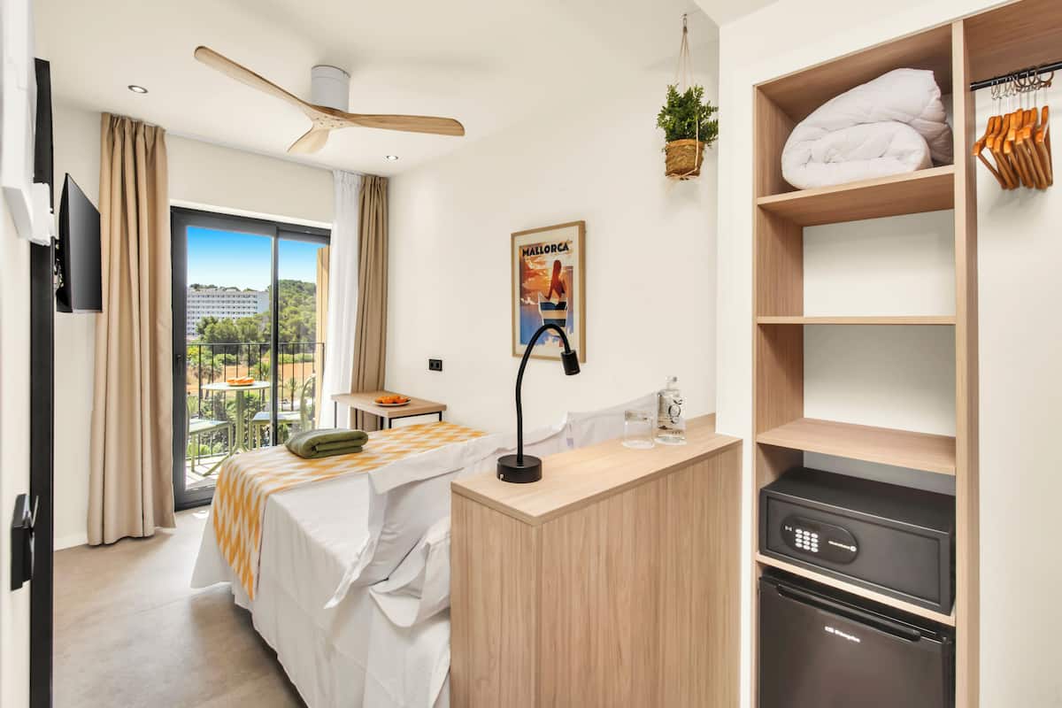 A hotel room with a bed, a desk with a lamp, a minibar, a TV, and a balcony with a view.