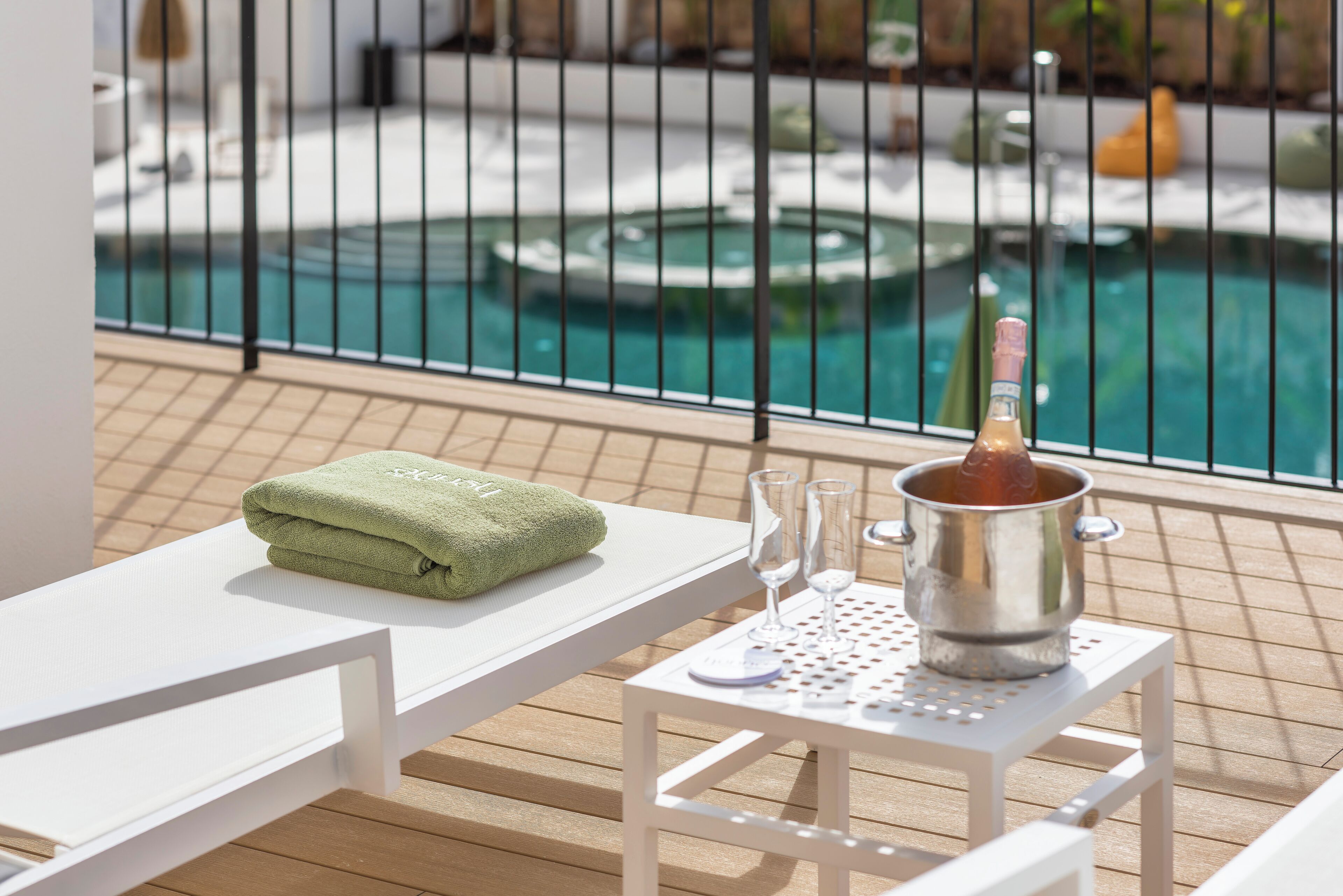 A poolside area with a white table, a green towel, and a champagne bucket.