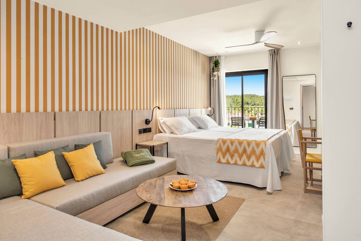 A modern hotel room with a bed, sofa, and a dining area.