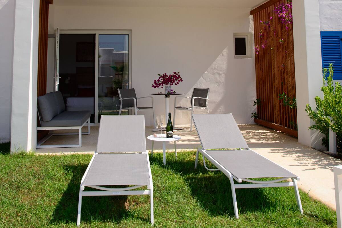 A modern building with a covered balcony, two lounge chairs, and a small table with a vase of flowers.