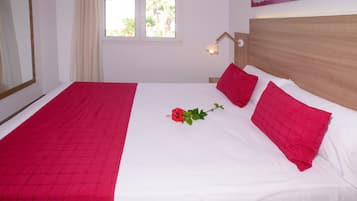 Una cama bien hecha con una colcha roja y blanca, una rosa roja solitaria y un cabecero de madera.