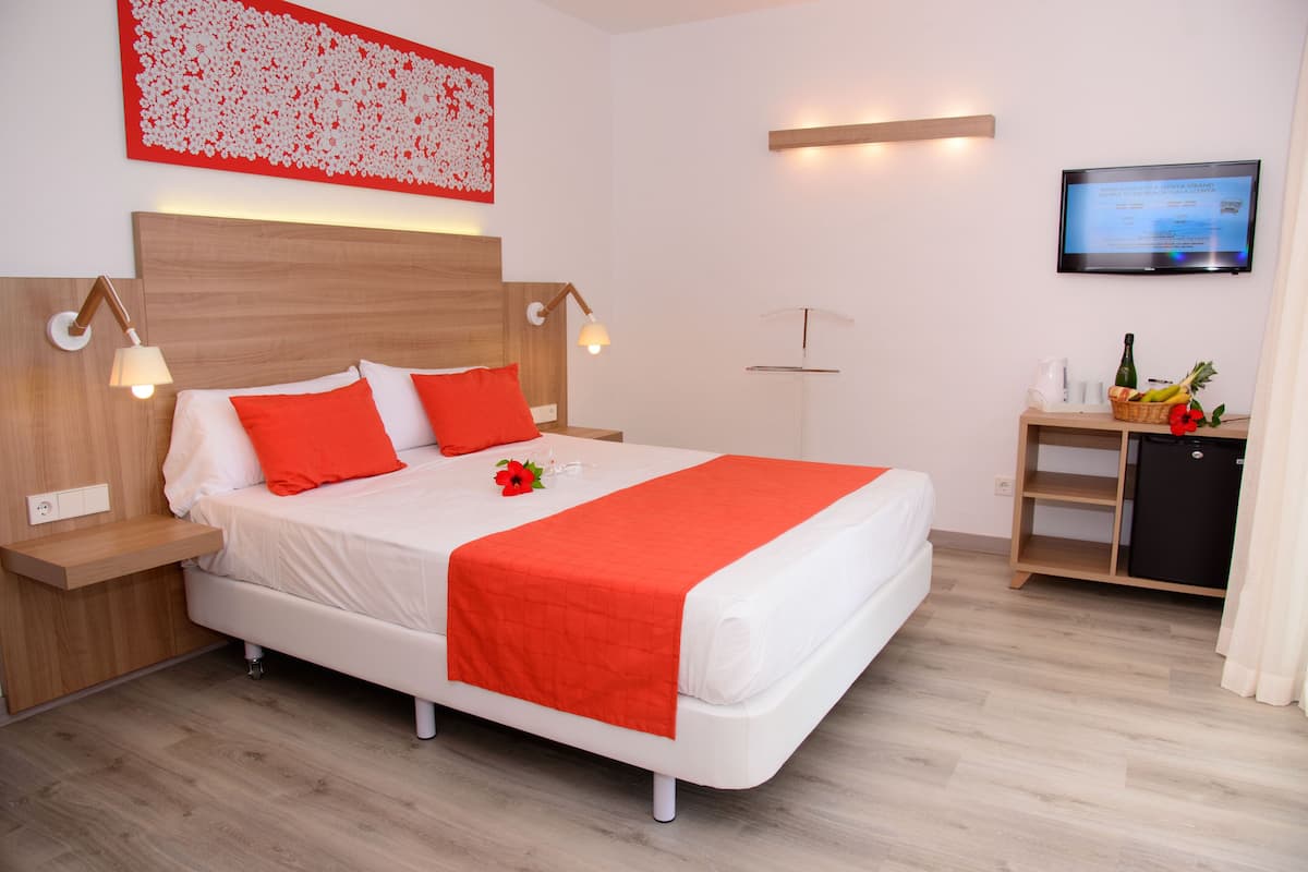 A modern hotel room with a neatly made bed, a flat-screen TV, and a small kitchenette area.