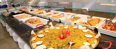 A buffet with various dishes, including a large pan of rice with vegetables and lemon slices.