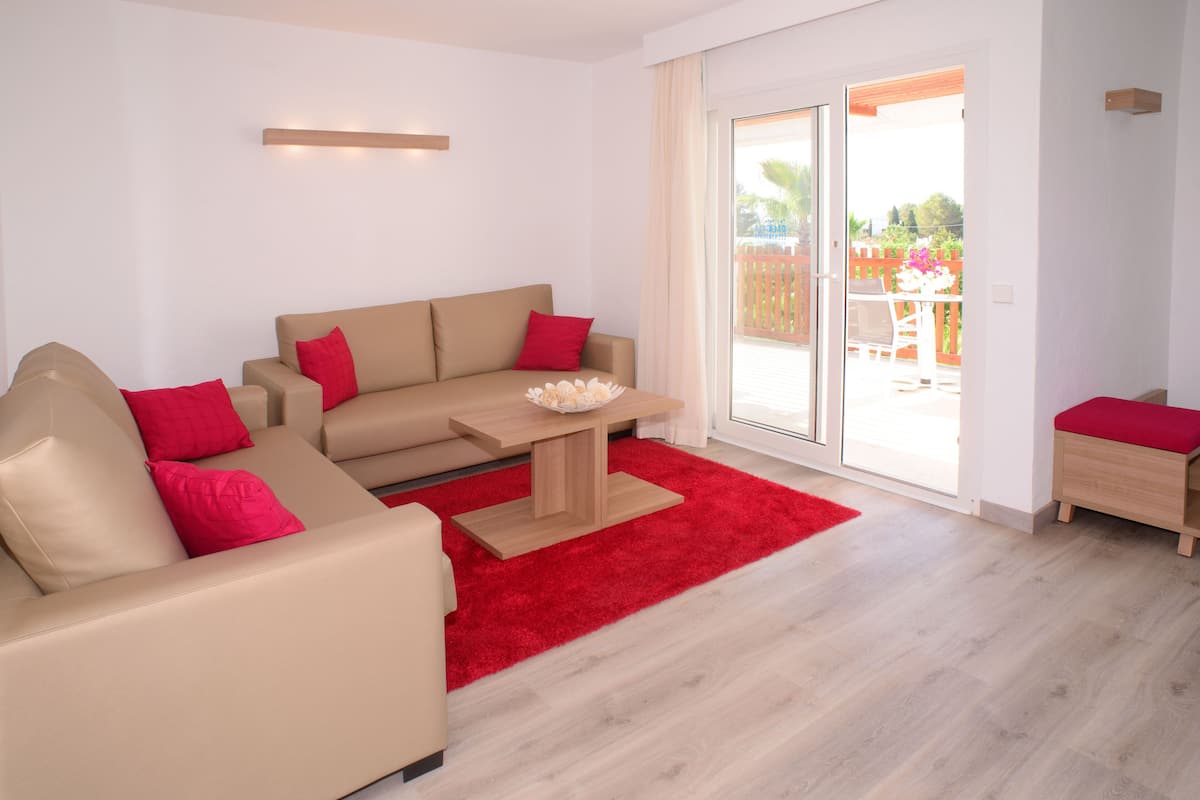 A modern living room with a beige sofa, red cushions, a wooden coffee table, and a red rug.