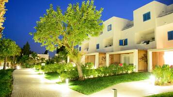 Un hotel moderno con paredes exteriores blancas, contraventanas azules y un camino bien iluminado que lleva a la entrada.
