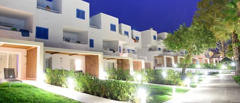 A row of white buildings with balconies, a pathway, and greenery.