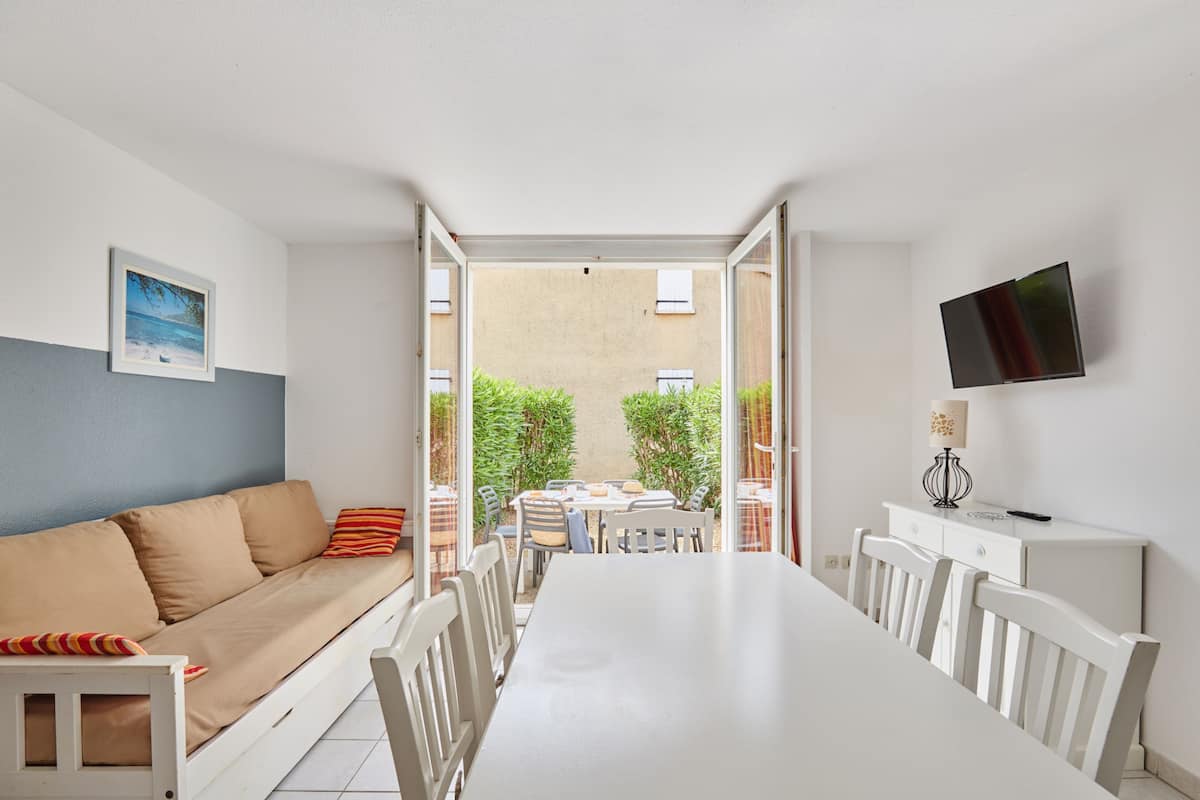 A room with a white sofa, a dining table, chairs, and a TV mounted on the wall.