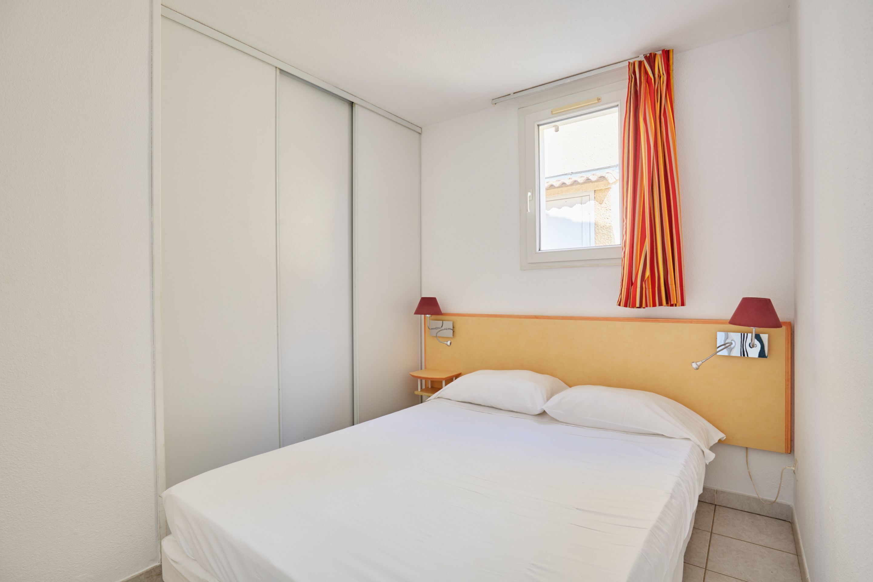 A hotel room with a bed, a nightstand, a lamp, a window with curtains, and a sliding door.