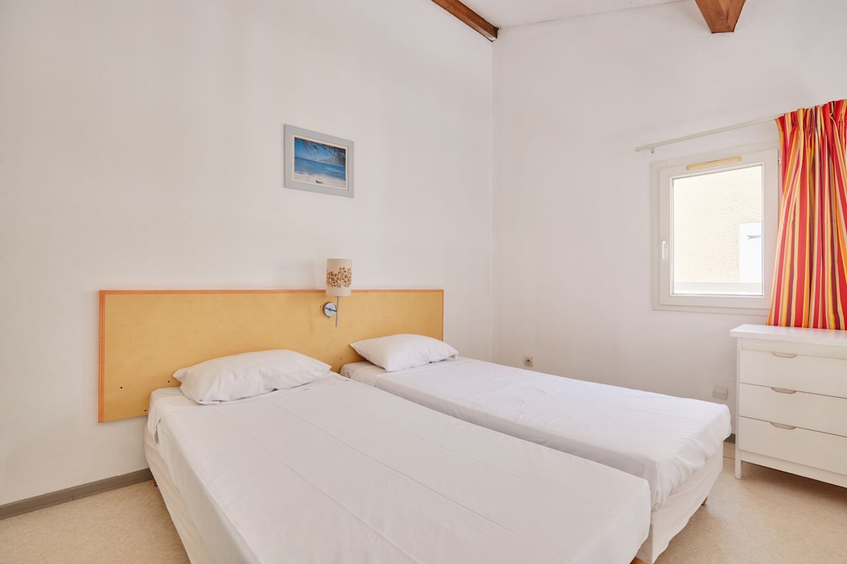 A room with two single beds, a white dresser, a window with curtains, and a framed picture on the wall.