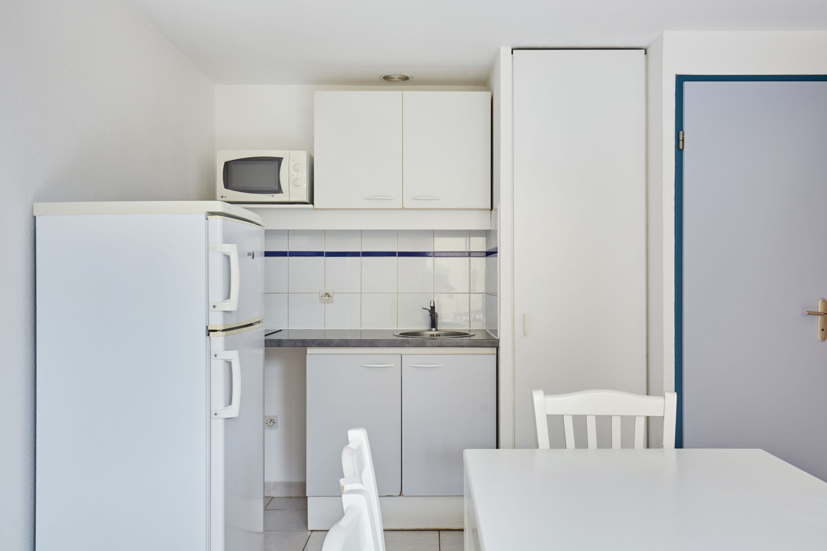 A compact kitchen with a refrigerator, microwave, and white cabinets.