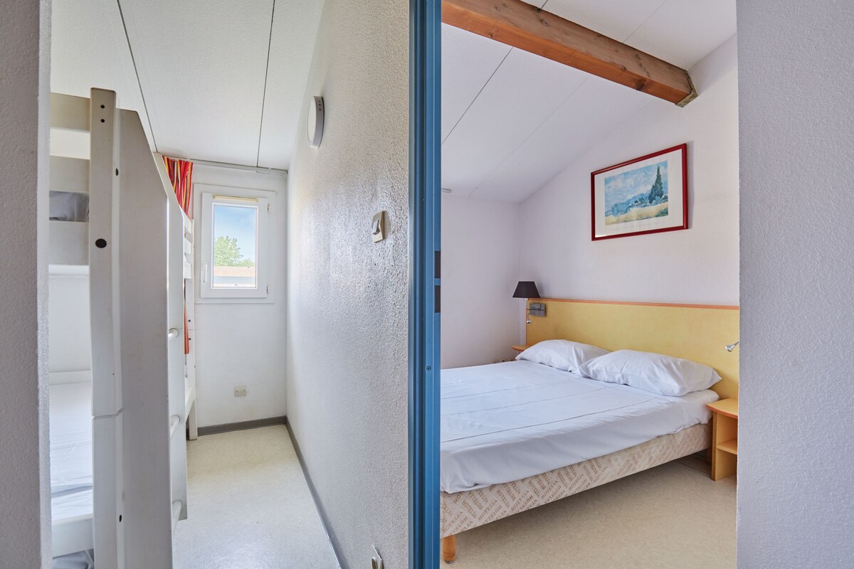 A bedroom with a bed, a nightstand, a window, and a door leading to another room.