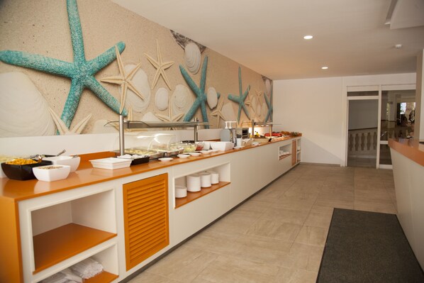Un espace buffet doté d’un long comptoir, de différents récipients contenant de la nourriture et d’un mur décoré d’étoiles de mer et de coquillages.