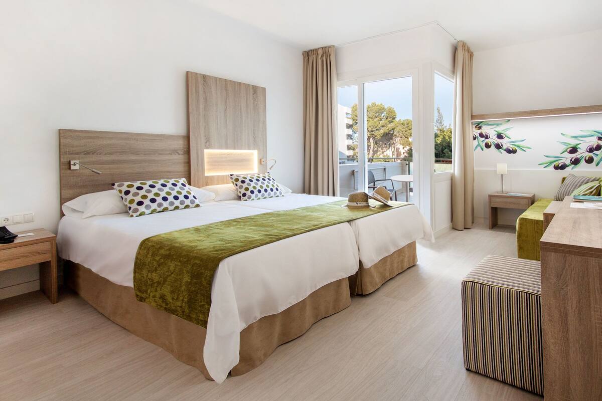 Une chambre d’hôtel moderne équipée d’un lit, de tables de chevet, d’un bureau et d’une grande fenêtre.
