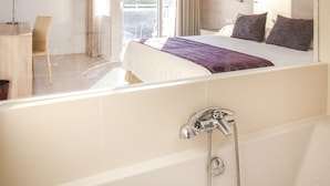 A modern hotel room with a large bed, a separate sitting area, a view of the city, and a bathtub. - Globales Hotel Maioris (Llucmajor)