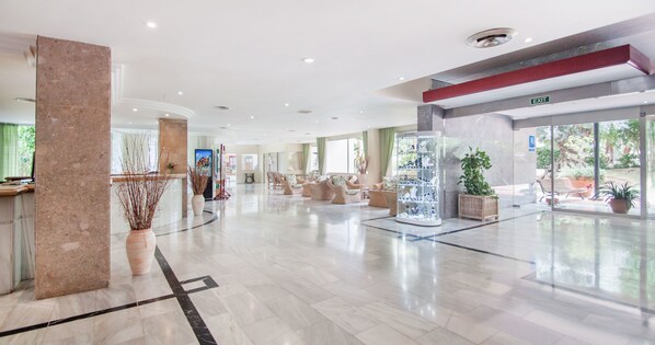 Un hall d’entrée spacieux avec un sol en marbre, un comptoir d’accueil, des coins salon confortables et une vitrine.
