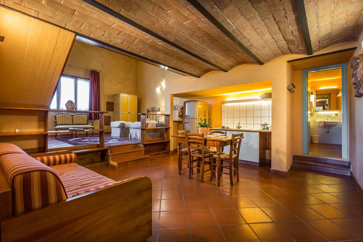 A cozy living room with a sofa, a dining table with chairs, a kitchen area with a sink, and a bathroom visible through an open door.