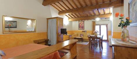 A room with a wooden bed, a wooden bench, a television, a sofa, and a dining table.