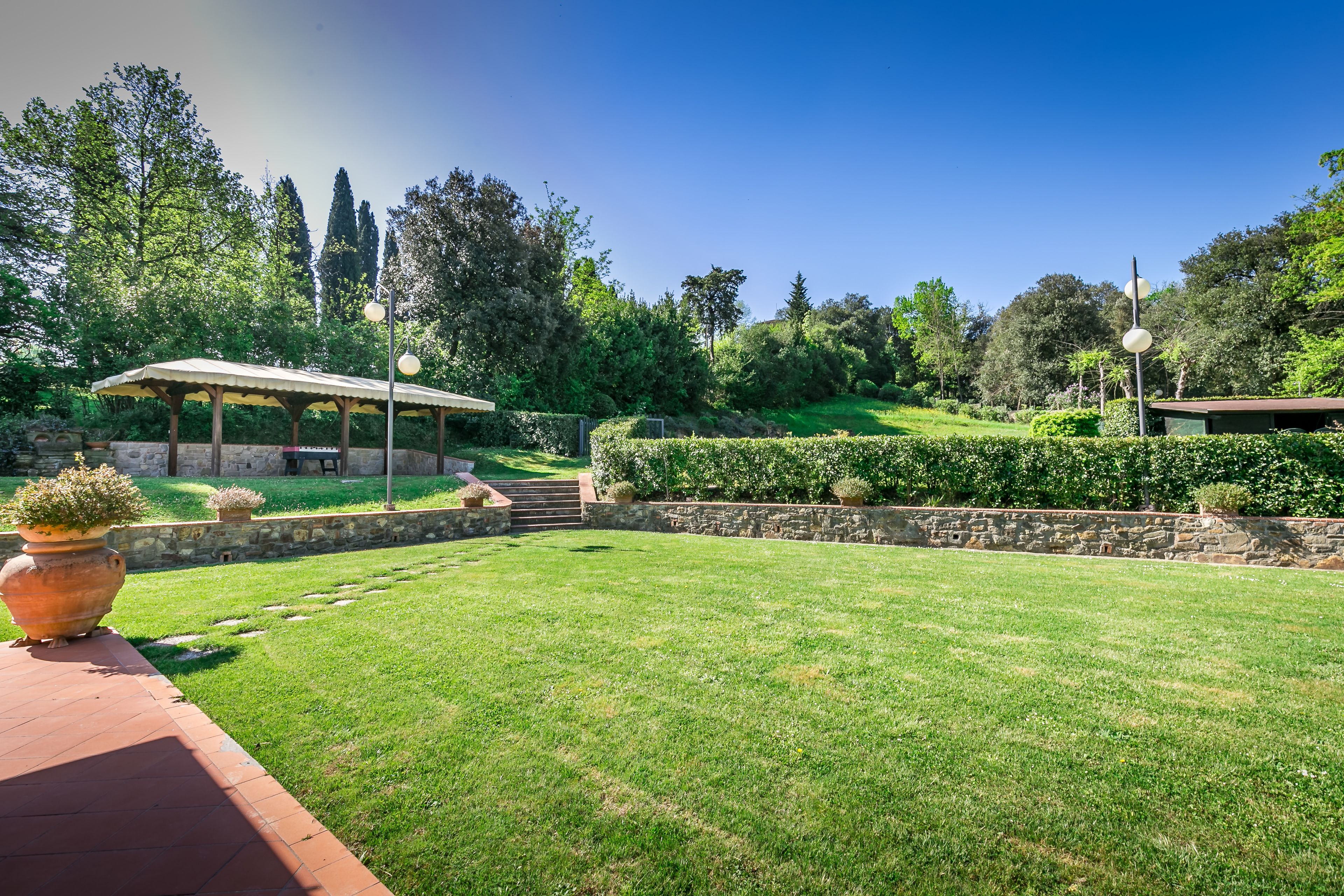 A well-maintained garden with a gazebo, stone walls, and a clear sky.