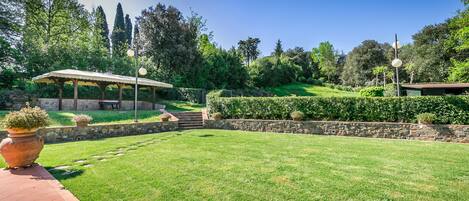 A well-maintained garden with a gazebo, stone walls, and a clear sky.