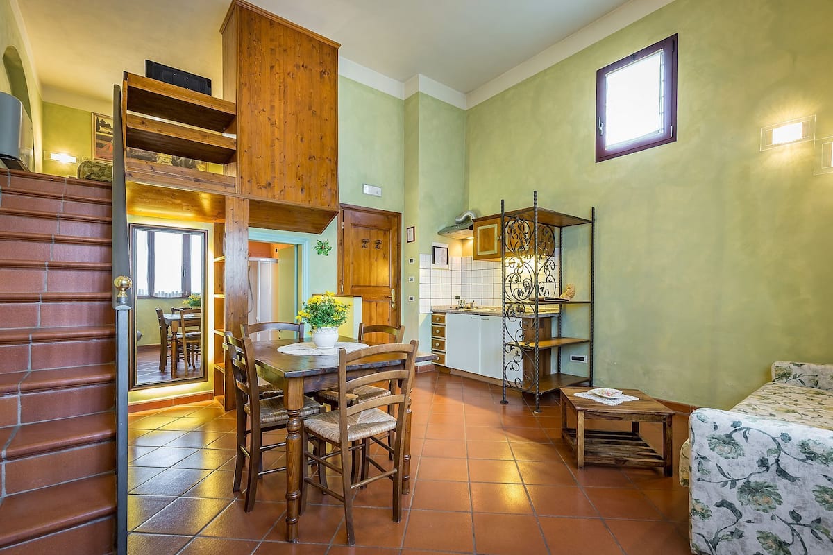 A compact kitchen with wooden cabinets, a dining area with a table and chairs, and a small seating area with a patterned sofa.