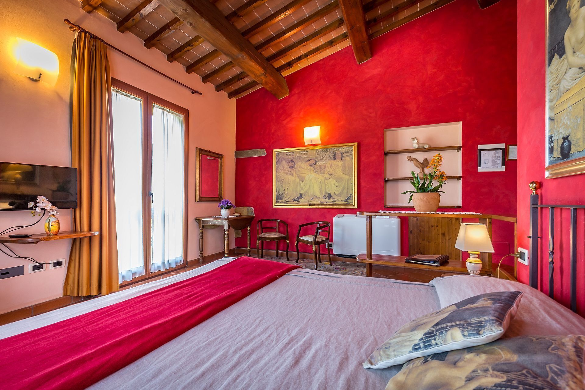 Une chambre d’hôtel avec un grand lit, un bureau avec des chaises, une télévision et un mur d’accent de couleur rouge.