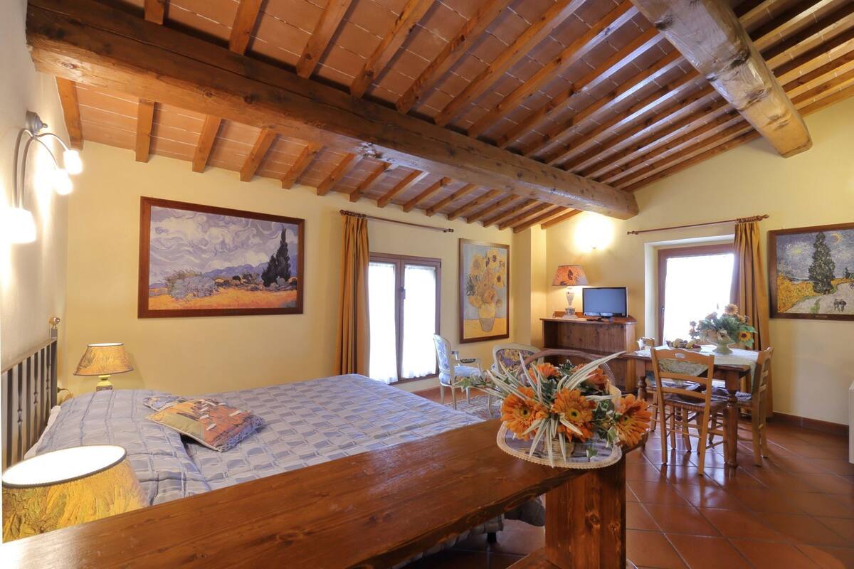 A room with a bed, a desk, a television, and artwork on the walls.
