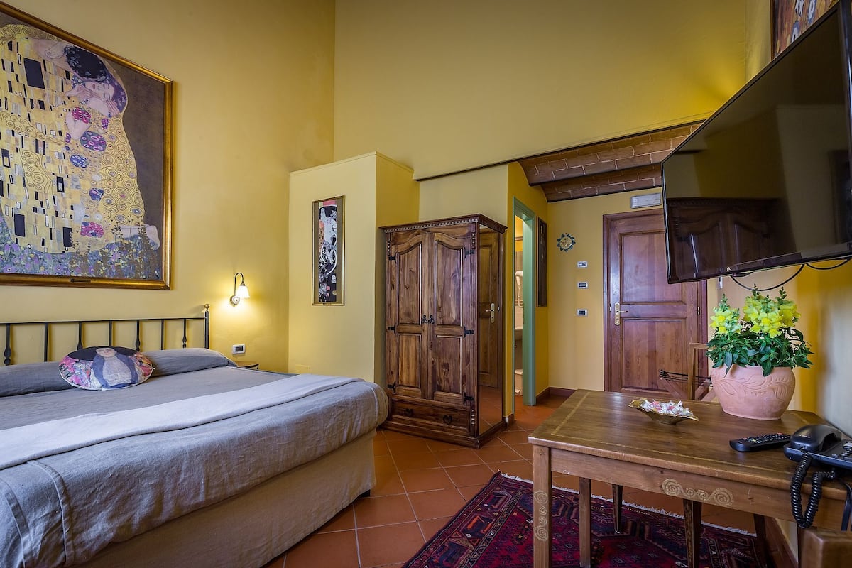 A bedroom with a bed, a wooden wardrobe, a desk with a telephone, and a television.