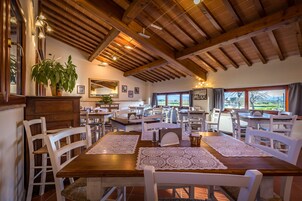 Un amplio comedor con mesas de madera y sillas blancas, ventanas grandes que ofrecen vistas y un techo con vigas a la vista.