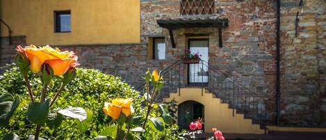 A building with a stone facade and a yellow wall, a staircase with a wrought iron railing, and a garden with roses.