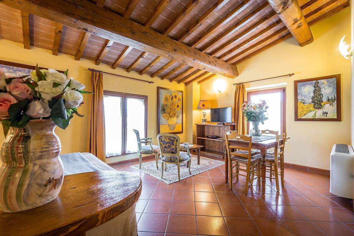 A spacious living room with a wooden ceiling, a dining area with a table and chairs, and a television on a wooden stand.