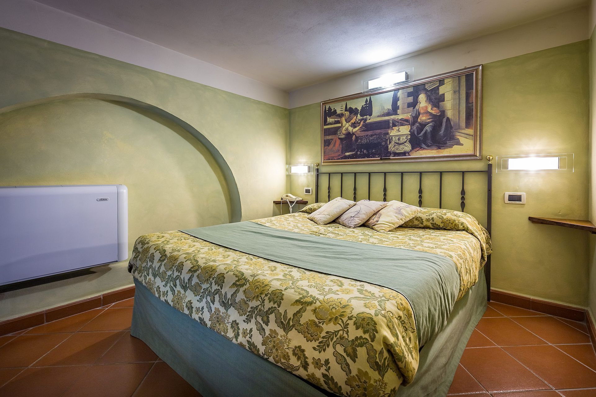 A bedroom with a bed, a painting on the wall, and a telephone on the nightstand.