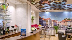 A hotel lobby with a bar area, seating, and a mural of a cityscape. - Hotel Gollner (Graz)