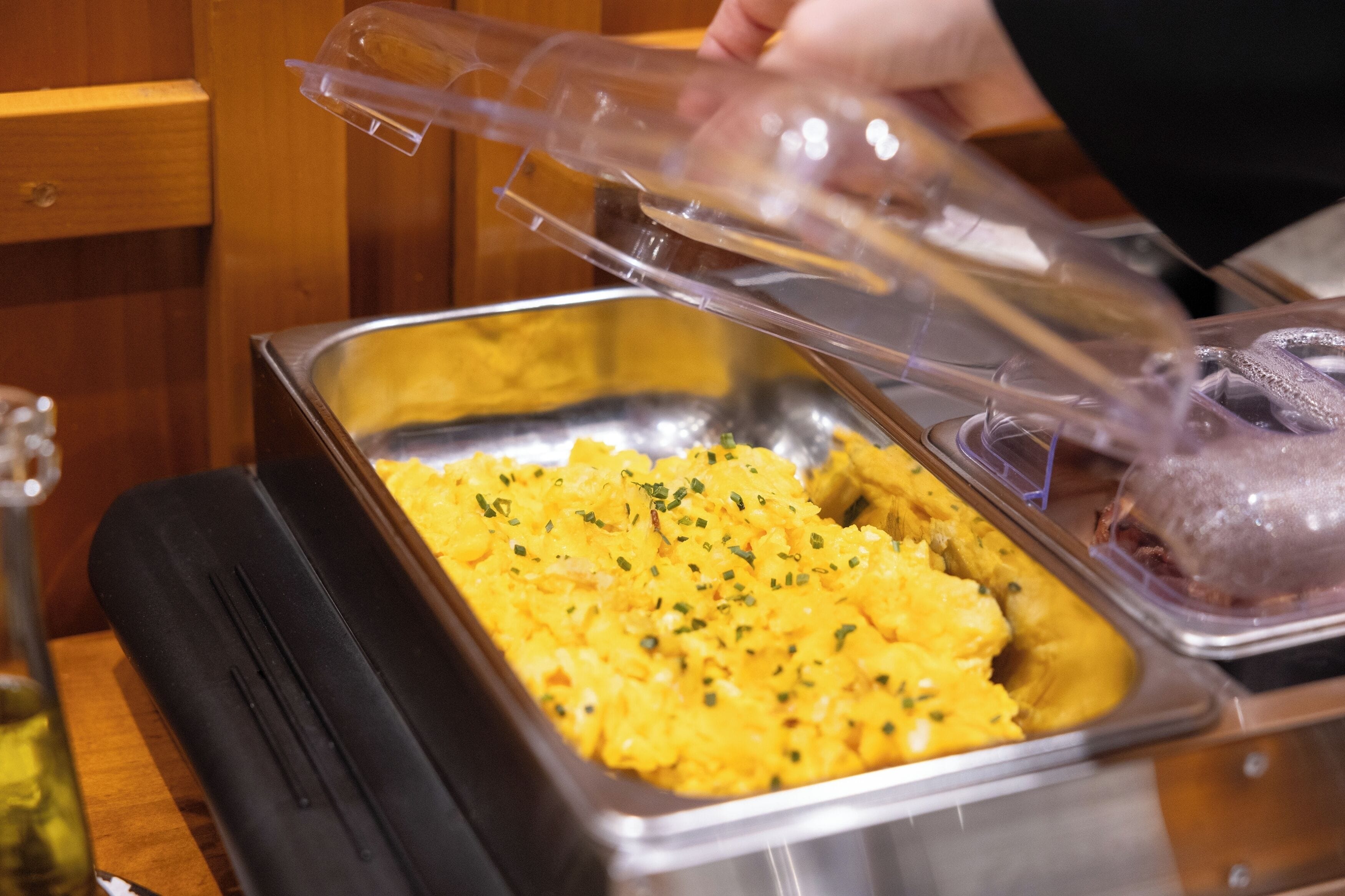 A buffet setup with a tray of yellow food and a plastic cover.