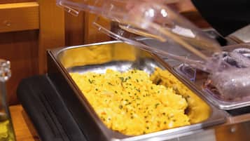 A buffet setup with a tray of yellow food and a plastic cover.