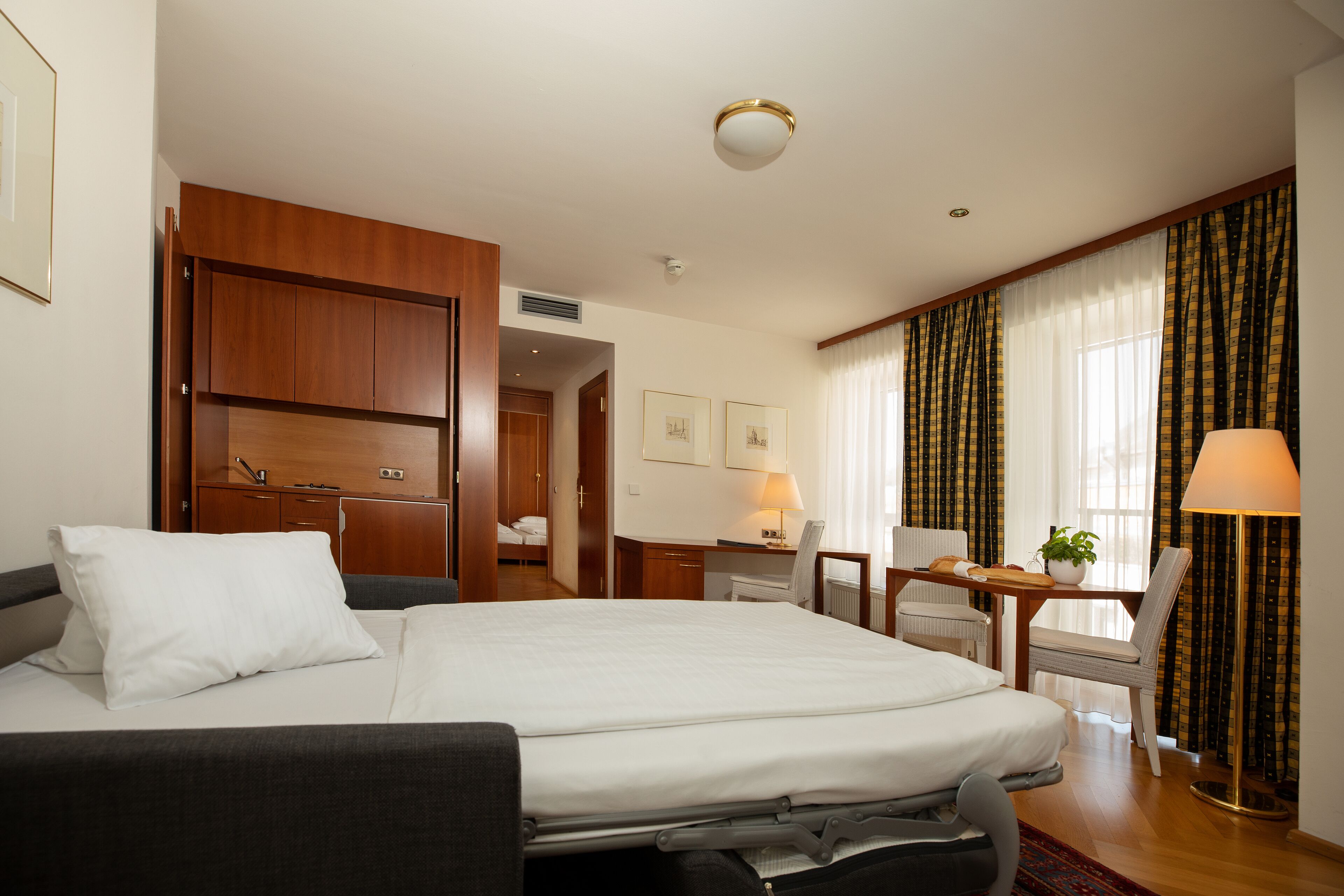 Habitación de hotel con una cama grande, un escritorio con silla, una mesita con una planta y una lámpara.